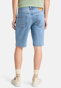 Pantalones cortos de denim azul claro con corte recto, que cuentan con dos bolsillos traseros y un parche de cuero en la cinturilla, combinados con zapatos blancos.