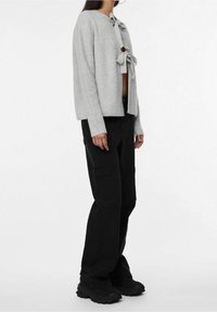 Cardigan grigio lavorato a maglia con scollo arrotondato e chiusura frontale a nodo, abbinato a pantaloni cargo neri con tasche laterali e gambe affusolate.