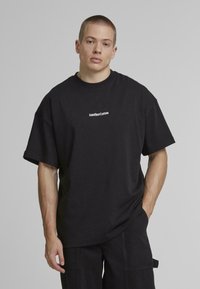 Sort bomulds t-shirt med korte ærmer, bred pasform og rund hals. Har hvid trykt logo "AnotherCotton" på tværs af brystet.