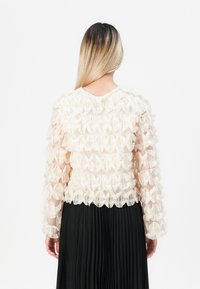 Top ruffled color crema con maniche lunghe, tessuto trasparente e design testurizzato. Abbinato a una gonna plissettata nera.