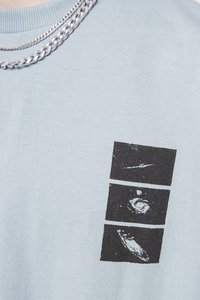 Light blue cotton t-shirt featuring a black graphic print of three abstract designs. Includes a crew neck and ribbed collar with silver chains.