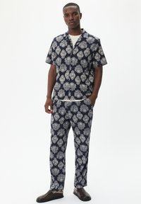 Camicia a maniche corte a fantasia navy e pantaloni coordinati presentano motivi floreali bianchi. L'outfit è realizzato in tessuto leggero con una vestibilità comoda.