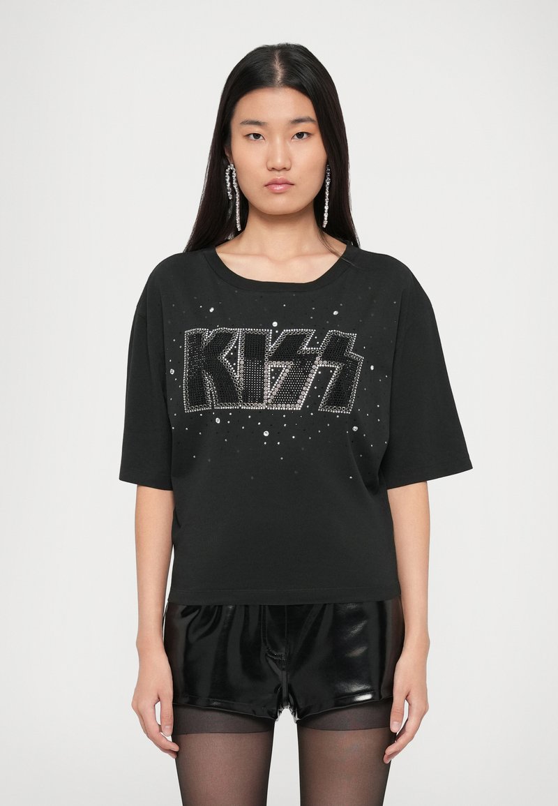 Black oversized t-shirt featuring a large "KISS" design in rhinestones, with short sleeves and a rounded neckline, worn with shiny black shorts.