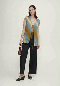 Bezrūmu, zils un dzeltenas svītrains tops ar mezgla aizdari priekšā; kombinēts ar melnajām platajām biksēm un melniem augstpapēžu sandaliem.