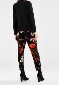 Svart åtsittande jacka med blommönstrade byxor i nyanser av röd, rosa och vit. Byxorna har manschettknappar och en mjuk textur.