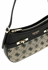 Sac à main noir et beige avec un corps en toile à motifs, des accents lisses, et une fermeture éclair ainsi qu'un logo en métal doré à l'avant.