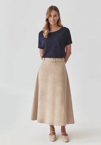 Marineblauw t-shirt met korte mouwen en een ronde halslijn, gecombineerd met een beige A-lijn maxi rok met een riem en een gladde stof. Beige schoenen maken de look compleet.