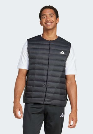 Czarna pikowana kamizelka z przeszyciami, zapinana z przodu na zatrzaski, z białym logo Adidas po lewej stronie klatki piersiowej. Nosi się ją na białą koszulę.