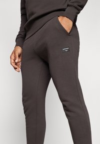 Braune Jogginghose mit schmaler Passform, aus weichem Stoff gefertigt. Verfügt über Seitentaschen und ein Markenlabel am unteren Bein.