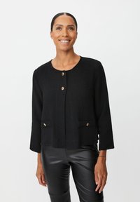 Zwarte geweven jas met een ronde halslijn, knopen aan de voorkant en twee decoratieve zakken. Voorzien van accenten in goudkleurige hardware. Slim fit ontwerp.