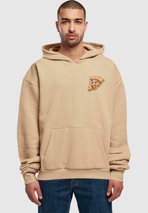 Beige Hoodie mit vorderer Tasche, oversized Schnitt, Kapuze mit Kordelzug und einer Pizza-Slice-Stickerei auf der linken Brust. Der Stoff wirkt weich.