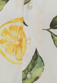 Tela blanca con rodajas de limón impresas y hojas verdes, que presenta un primer plano de tres botones de crema cosidos.
