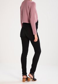 Suéter recortado de color rosa claro, jeans ajustados negros, sandalias negras de tacón con detalle de hebilla. Textura suave, diseño ajustado y silueta elegante.