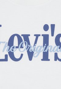 Λευκό βαμβακερό t-shirt με μεγάλο μπλε κείμενο "Levi's" και την υπογραμμισμένη λέξη "The Original" με καλλιγραφικό στιλ, παρουσιάζοντας ομαλή υφή και έντονο σχέδιο.