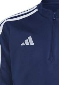 Giacca zip-up blu navy realizzata in tessuto testurizzato, con strisce bianche sulle spalle e il logo bianco di Adidas sul lato sinistro del petto.