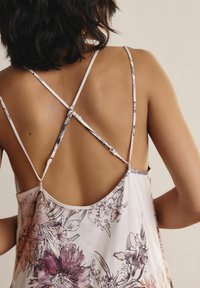 Camisola floreale leggera con scollatura bassa, caratterizzata da sottili spalline incrociate sul retro, in morbidi colori pastello con motivi floreali scuri.