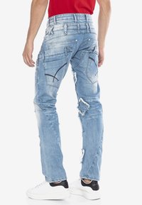 Helle blaue, abgenutzte Denim-Jeans mit geradem Schnitt, mehreren Taschen und kontrastierenden Nähdetails. Kombiniert mit weißen Sneakers.