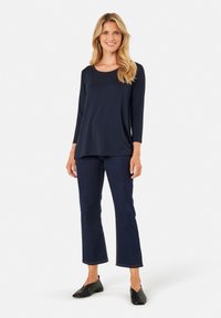 Navyblaues Langarmshirt mit Rundhalsausschnitt, kombiniert mit ausgestellten dunklen Jeans und schwarzen Slippern. Glattes Material, lockere Passform.