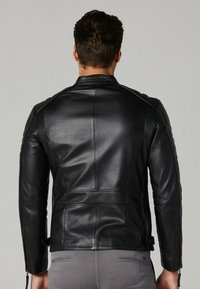 Zwarte leren jas met een slank design, voorzien van gevoerde schouderaccenten en ritssluiting aan de mouwen. Glad textuur met gestikte details.