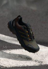 Scarpa da hiking nera e verde oliva con tomaia in rete, suola in gomma e dettagli gialli. Presenta tre strisce e punta rinforzata.