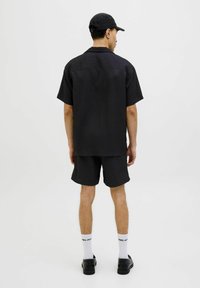 Chemise à manches courtes rayée noire avec un short assorti, tous deux en tissu texturé. Porté avec des chaussures noires et des chaussettes blanches, vu de l'arrière.