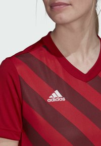 Rotes Sporttrikot mit diagonalen Streifen, aus atmungsaktivem Material. V-Ausschnitt mit weißem Adidas-Logo auf der linken Brust.