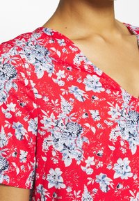 Haut à motif floral rouge avec un décolleté en V, des manches courtes et un tissu texturé doux agrémenté de fleurs bleues et blanches.