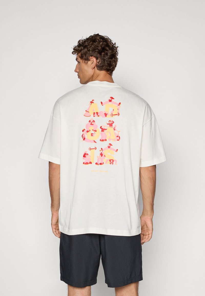 Lys kremfarget oversized t-skjorte med fargerik grafisk tekst på baksiden, med avslappet passform og korte ermer. Kombinert med mørke shorts.