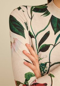 Long-sleeve top in light beige with a floral print. Features green leaves and pink flowers, made of a smooth, stretchy fabric.