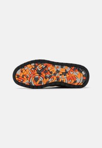 Semelle de chaussure avec bord noir et motifs géométriques abstraits orange vif, gris et noir ainsi que des zones de grip texturées.