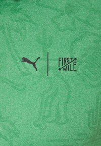 Tissu vert texturé présentant un logo Puma noir et le texte "FIRST MILE", centré de manière proéminente avec des lignes horizontales, sur un fond vert vif.