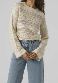 Sweter dziany w jasnym beżu z otwartym wzorem, z brzegiem w rib oraz rozszerzanymi rękawami, w zestawie z dżinsami z wysokim stanem.