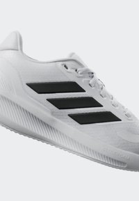 Chaussure de sport blanche avec une tige en mesh texturé, trois rayures noires diagonales et une semelle extérieure en caoutchouc comportant des rainures prononcées et le marquage "Cloudfoam".