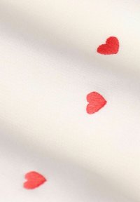 Witte stof met een gladde textuur, versierd met kleine rode geborduurde hartjes die over het oppervlak verspreid zijn.