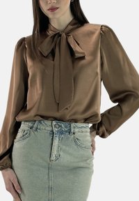 Brun satinbluse med bundet sløjfe i halsen, puffede ærmer og en glat tekstur, kombineret med en lyseblå denim pencilnederdel.