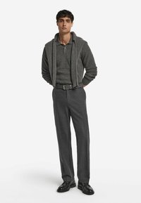 Grå ribbad polo shirt med sjalkrage, kombinerad med mörkgrå skräddarsydda byxor och svarta skor, och en bälte med rektangulärt spänne.