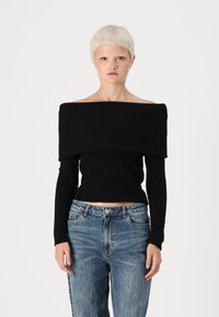 Schwarzes, trägerloses, geripptes Oberteil mit langen Ärmeln, kombiniert mit hellblauen, lässigen Jeans. Der Stoff wirkt weich und strukturiert.