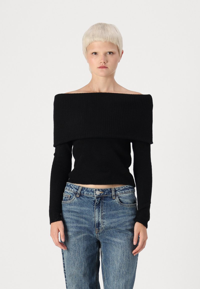 Schwarzes, trägerloses, geripptes Oberteil mit langen Ärmeln, kombiniert mit hellblauen, lässigen Jeans. Der Stoff wirkt weich und strukturiert.