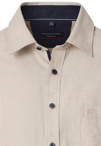 Beige casual-fit shirt met een gestructureerd patroon, donkere knopen en een klein borstzakje; de binnenkant van de kraag is donkernavy blauw.