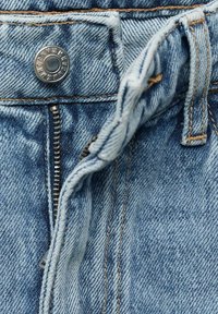 Jean en denim bleu clair avec une fermeture éclair argentée ouverte et un bouton en métal portant l'inscription "MNGDN & MNG".