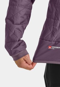 Purple quilted jacket with textured fabric, featuring a gray cuff. A logo reading "SWISSWOOD INSIDE" is visible on the lower hem.