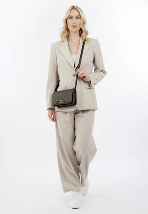 Beige maatpak met losse broek en een blazer met één knoop, gecombineerd met een gestreepte schoudertas en witte sneakers.