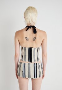 Top corsetto beige a righe con un fiocco nero al collo, abbinato a pantaloni corti coordinati. Presenta tatuaggi a forma di farfalla sulla schiena.