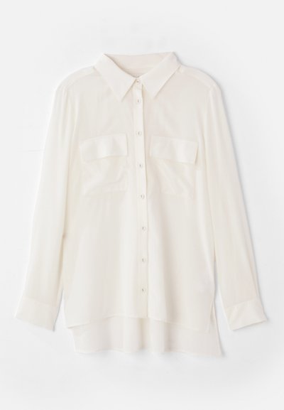 Camicia bianca a maniche lunghe realizzata in tessuto leggero. Presenta un colletto classico, due tasche sul petto e un orlo posteriore leggermente più lungo.