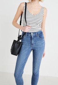 Top de tirantes de rayas en blanco y azul marino combinado con jeans de mezclilla azul de tiro alto y un bolso cruzado de cuero negro.