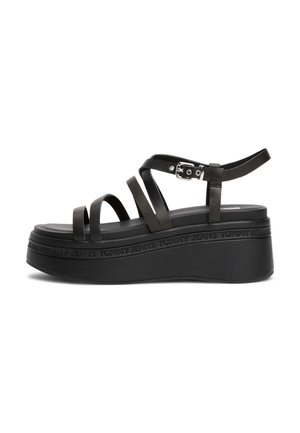 Sort platformsandal med flere tynde remme og en sølvspænde, med præget tekst "Tommy Jeans" rundt om sålens kant.