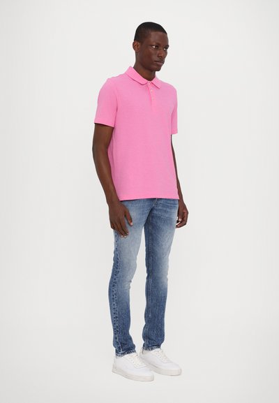 Polo shirt rose à manches courtes avec col et patte de boutonnage à trois boutons, associé à un jean skinny bleu clair délavé et des baskets blanches.