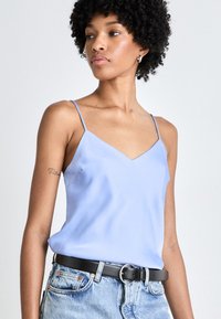 Camisola de satin albastră deschisă cu decolteu în V, bretele subțiri și croi lejer, asortată cu pantaloni scurți din denim cu talie înaltă și o curea neagră.