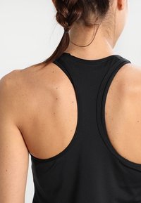 Schwarzes sportliches Tanktop mit Racerback-Design. Aus glattem, leichtem Stoff, mit sichtbaren Nähten und einer taillierten Silhouette.