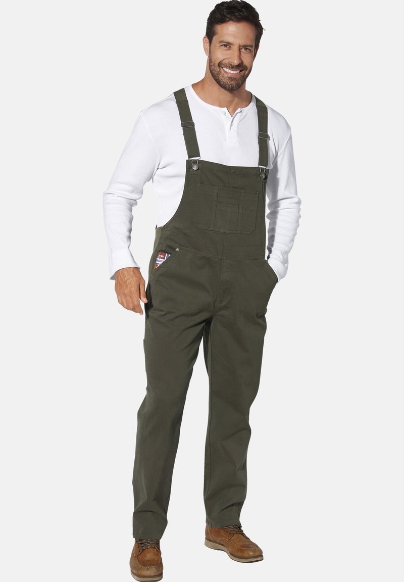 Olivgrüne Latzhose aus strapazierfähigem Stoff, mit verstellbaren Trägern, Vordertaschen und Metallbeschlägen. Gestylt mit einem weißen Langarmshirt.